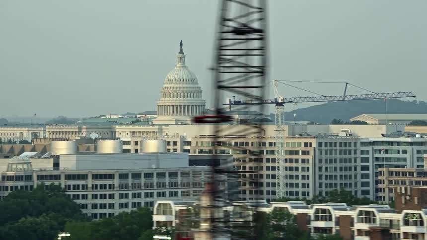 Aerial footage of the United States Capitol dome at sunset in Washington DC with office buildings and construction cranes in the background