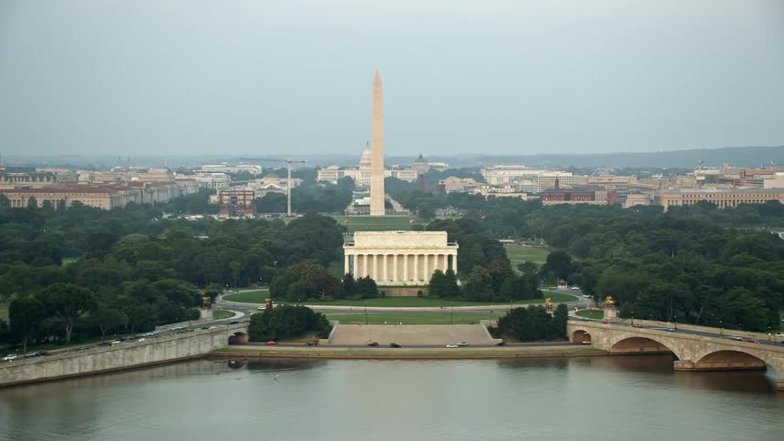 Cars crossing Arlington Memorial Bridge towards the Washington Monument during sunset in aerial stock footage of Washington DCs historical landmarks