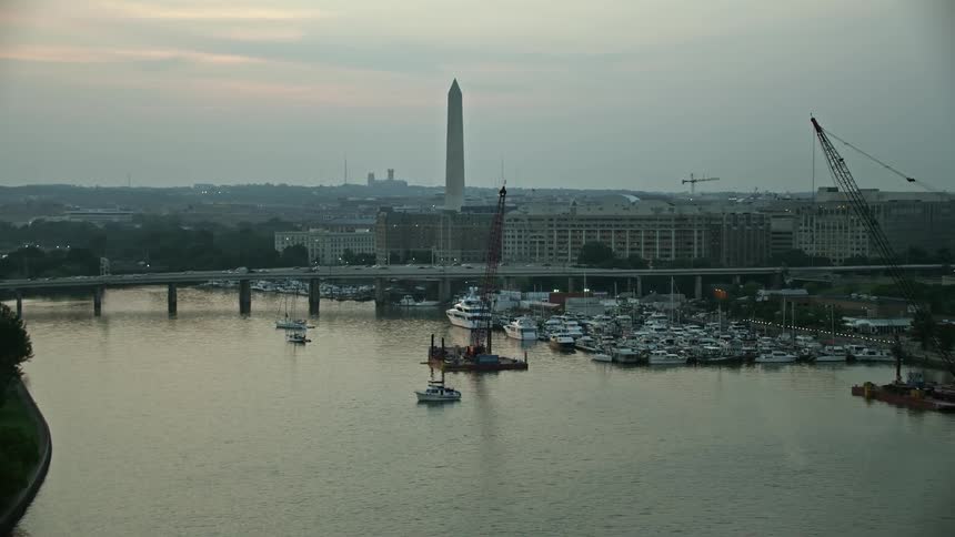 Aerial footage of the Francis Case Memorial Bridge and Washington Monument in Washington DC at twilight with a marina and fog covered monument in the distance as traffic crosses the river nearby