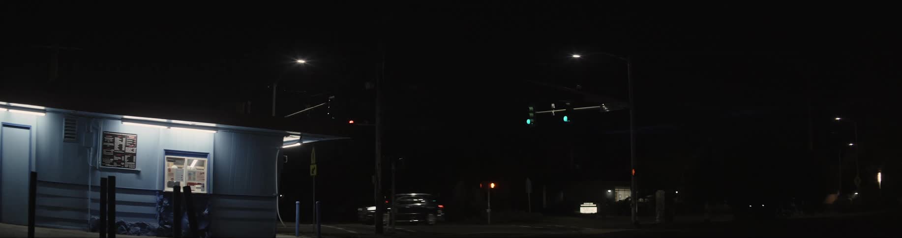 A blue building lit up at night with cars passing by on the road behind it