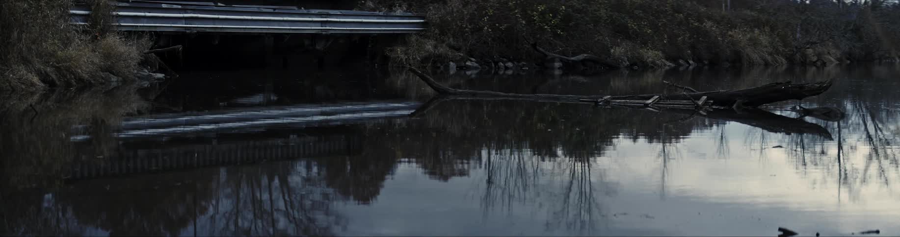 Swampy water sitting with the reflection of the shoreline and a car driving by