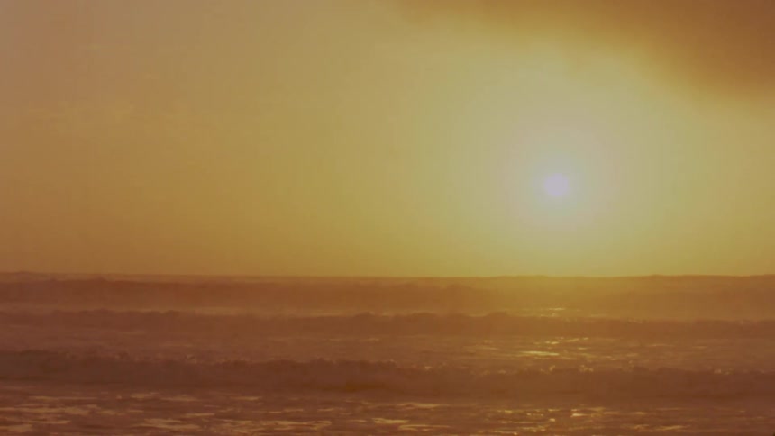 Ocean waves wash in and out from a beach at sunset
