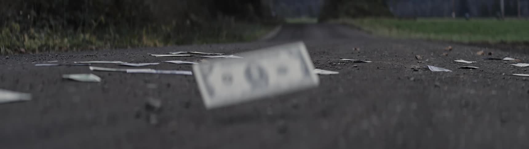 Dollar bills blowing around on a deserted road