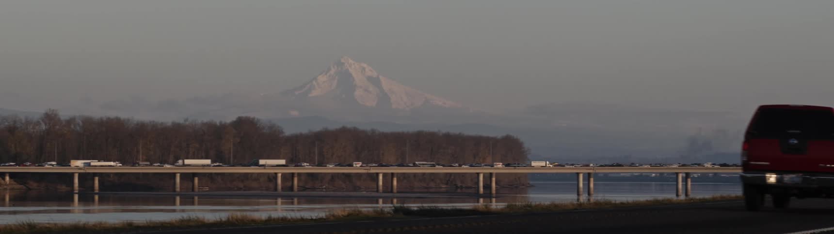 Landscape of cars driving on highway and bridge with distant snowy mountain in the background