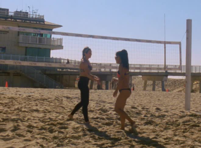 Two women walking on a sand volleyball court slapping hands and smiling