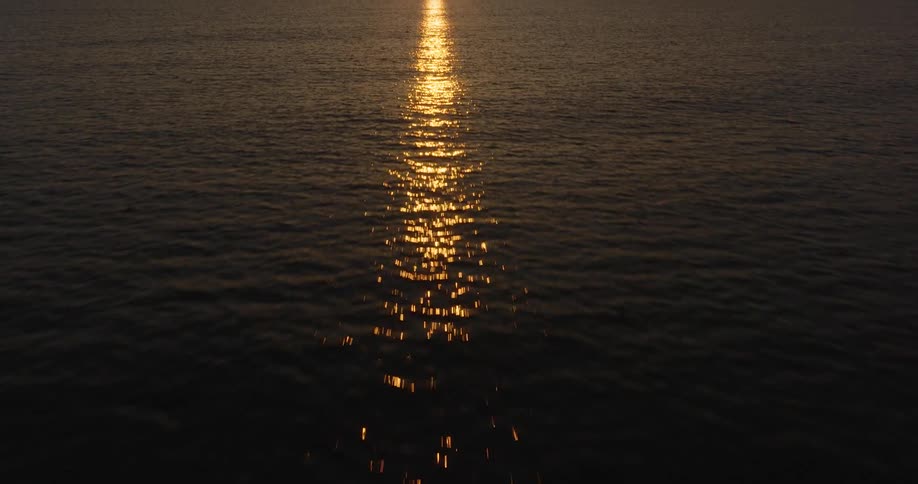 Camera flies over ocean and tilts up to see the sunset beyond