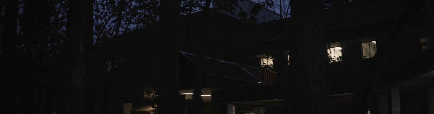 A silhouette of a house at night with a few lights on inside