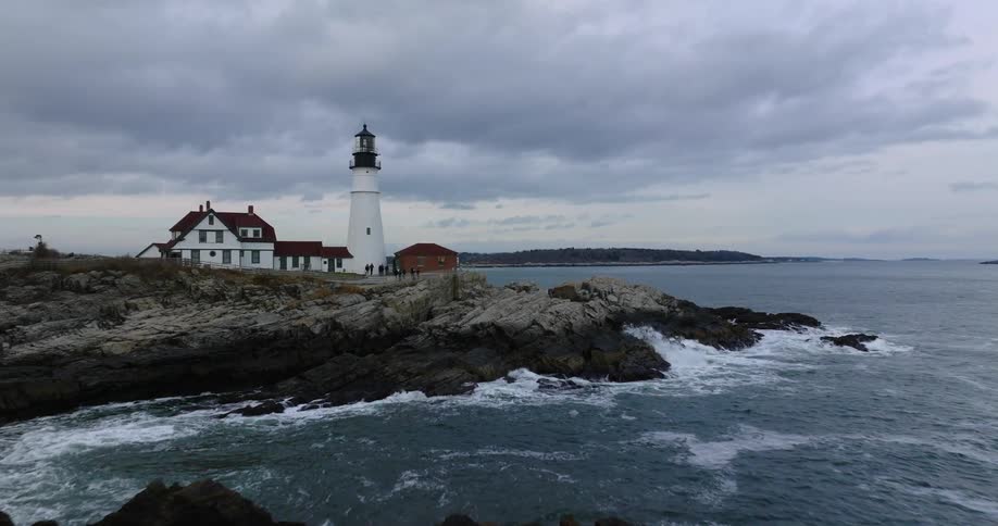 Camera soars in toward white lighthouse as tourists gather around it