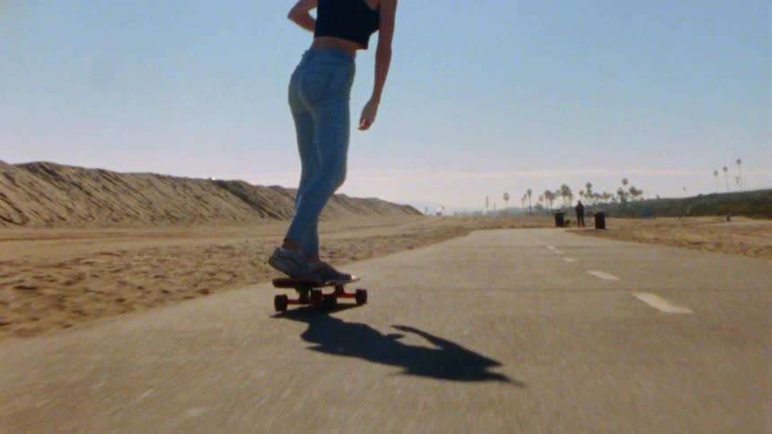 A teenage girl is riding a skateboard on a road through the beach