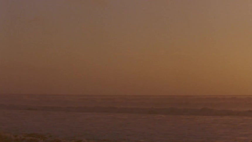 A beach with waves against a smog covered sunlit sky