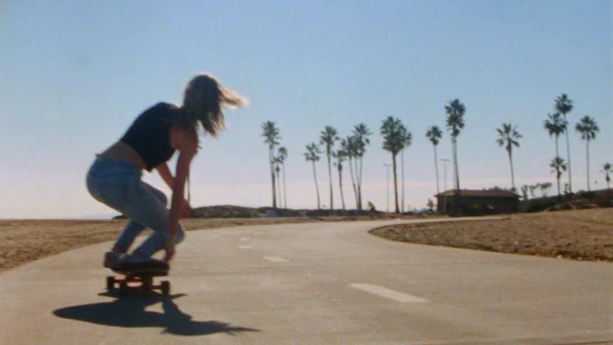 A woman stands up while riding her skateboard on the beach