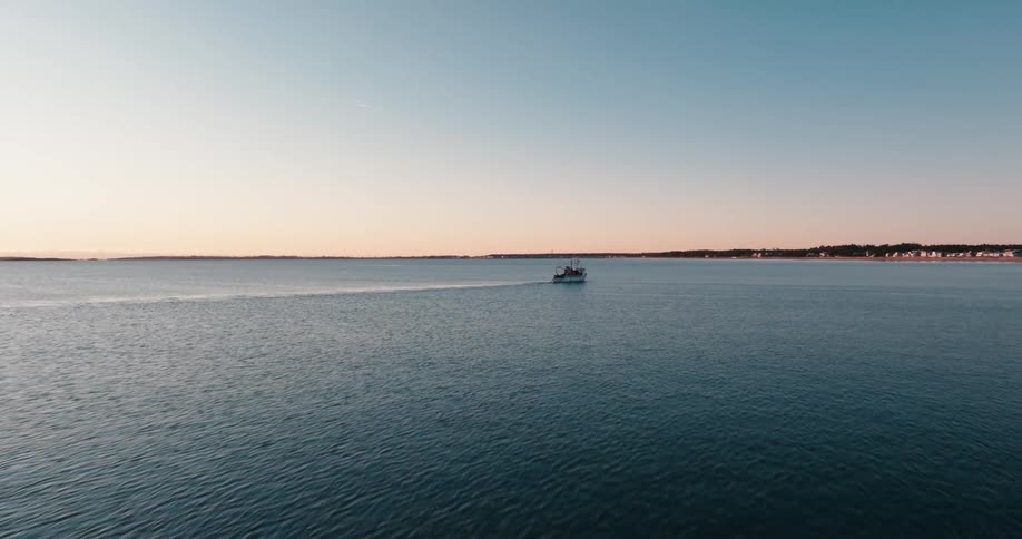 Camera flies over a fishing boat returning to port at sunrise