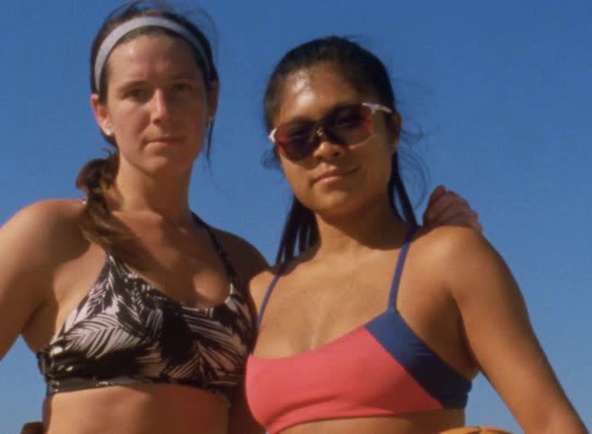 Two friends wearing swimsuits hugh each other looking at the camera