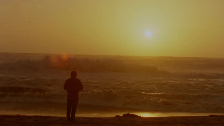 Silhouette of a man standing on a beach in front of the ocean at sunset