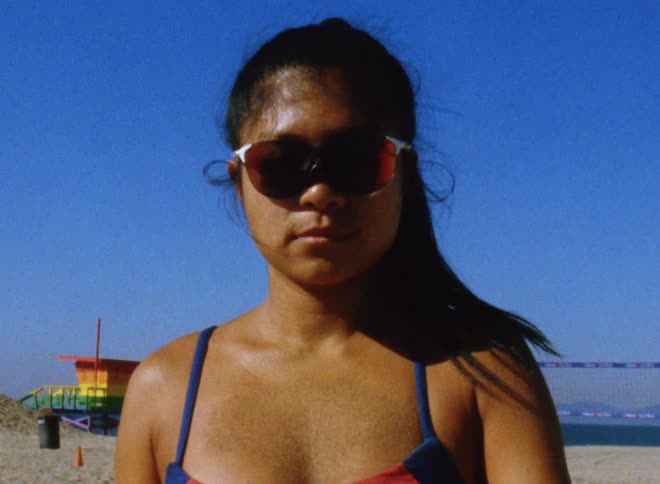 A teenage girl wearing sunglasses and a swimsuit is standing on the beach