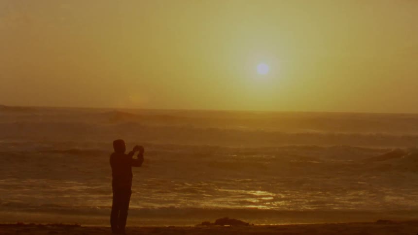 Silhouette of a man taking pictures on a beach in front of the ocean at sunset