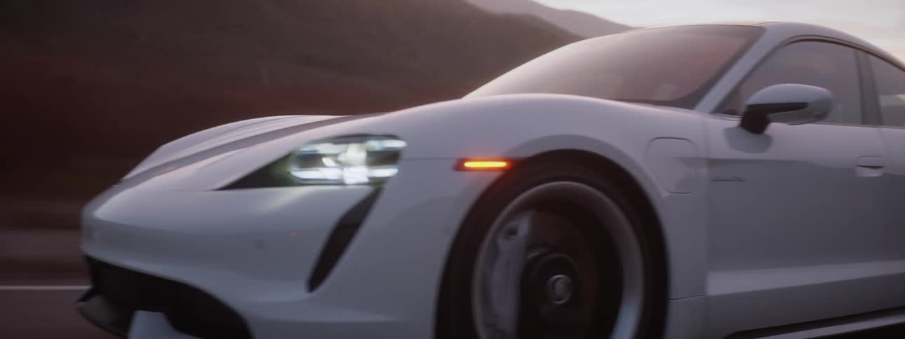 A white sports car races down a highway with mountains in the background