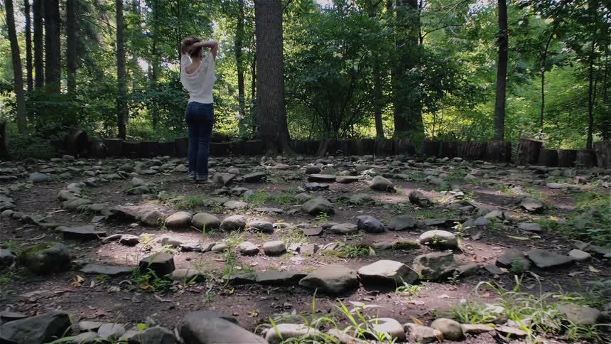 A woman walks along the rocks near a forest