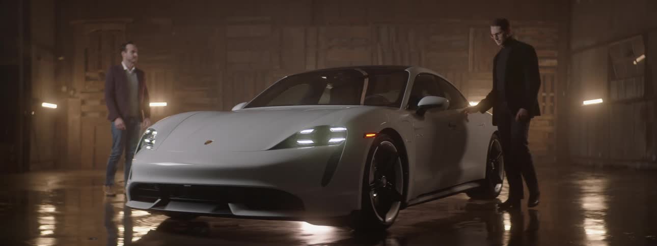Two men are standing in a garage looking at a white sports car as one of the men gives the other the keys and he walks around the car as the headlights come on and the garage lights flash and he gets in the drivers seat and closes the door