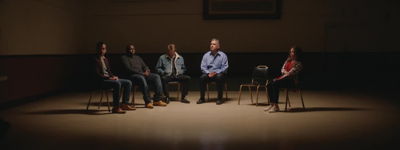 A group of six people are sitting in a row of chairs and two people decide to get up and walk away