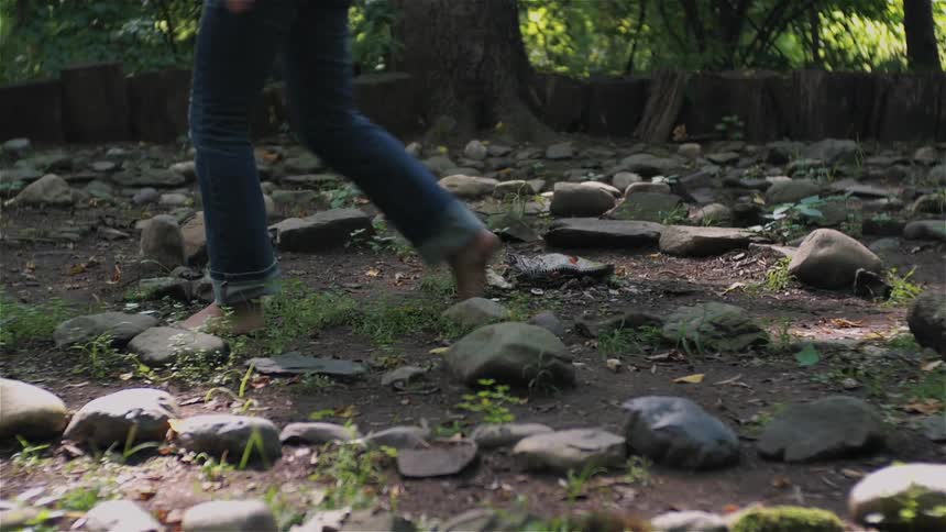 A woman is crouched by some rocks before getting up and walking