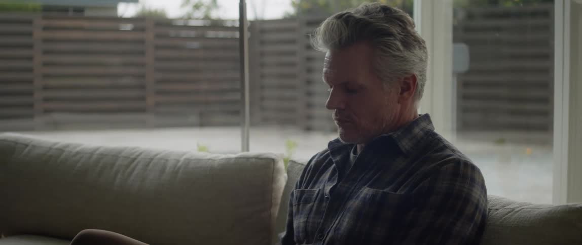 Man sitting on a couch at home near the windows looking at the backyard