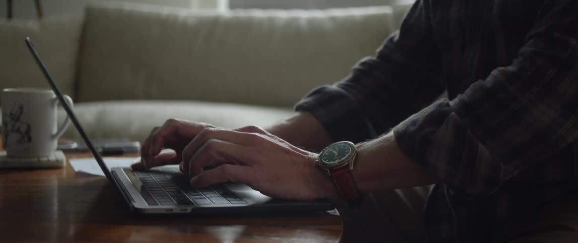 A man wearing a watch types on a laptop