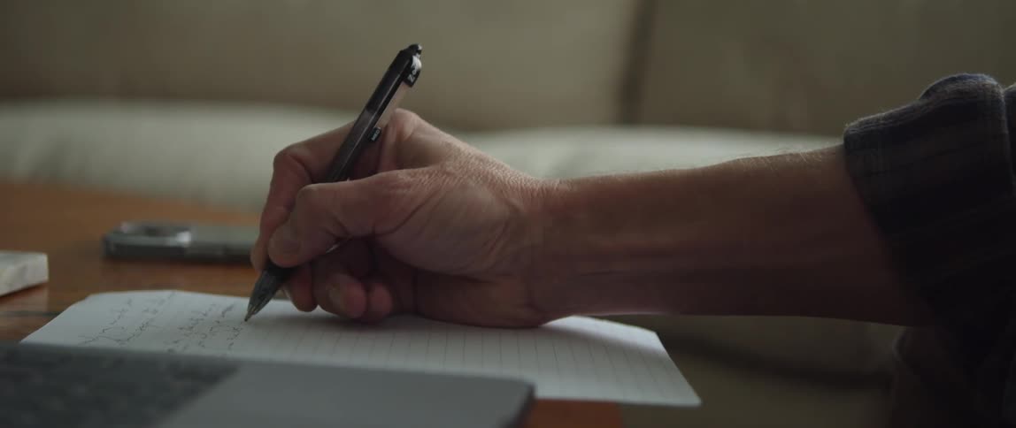 A person writing with a pen on a piece of lined paper