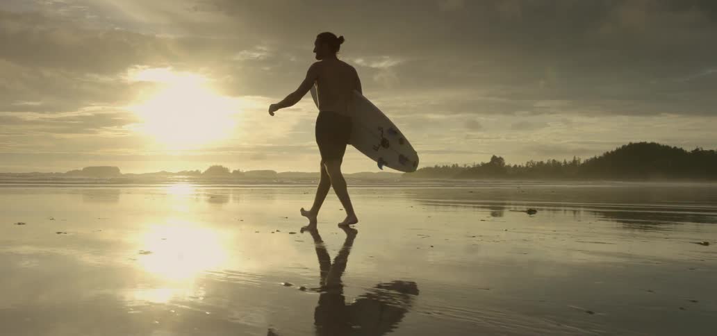 Surfer walking along a beach with his board at sunset