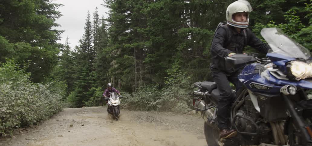 Motorcyclists riding through puddles on a dirt road in the forest