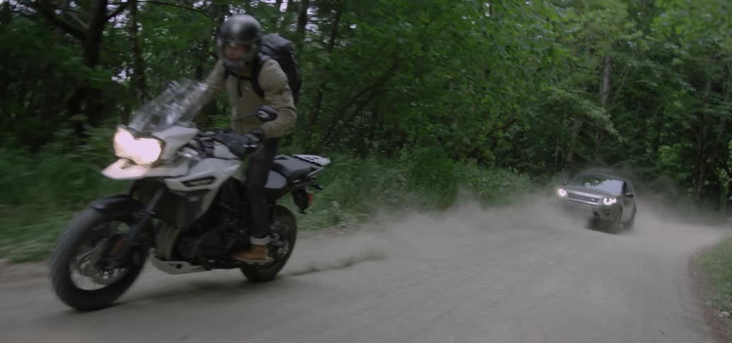 A motorcycle is followed by a car on a dirt road