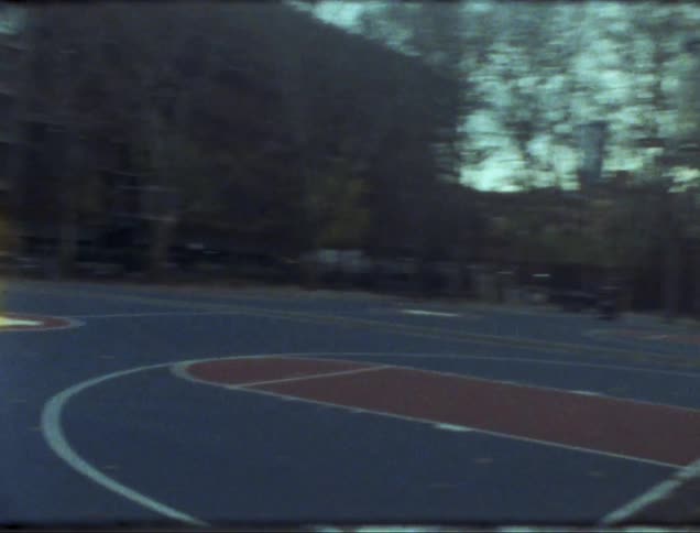 A basketball court is surrounded by trees and a nearby building