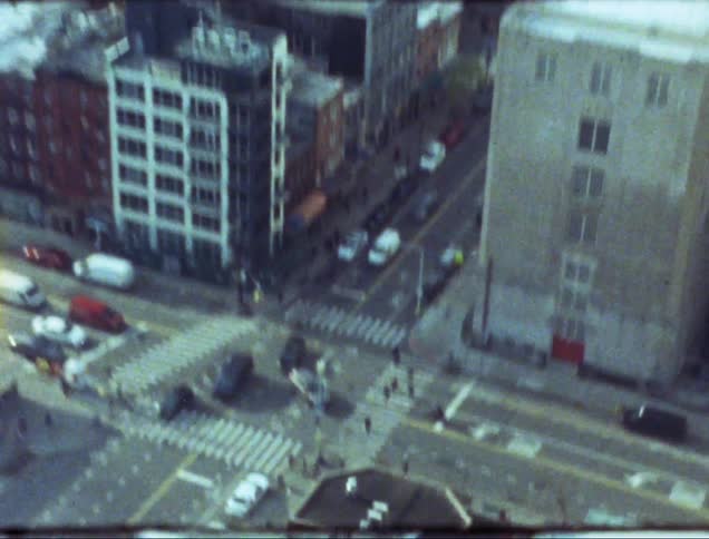A zoomed in shot of an intersection with people walking across it and then zoomed out onto the city