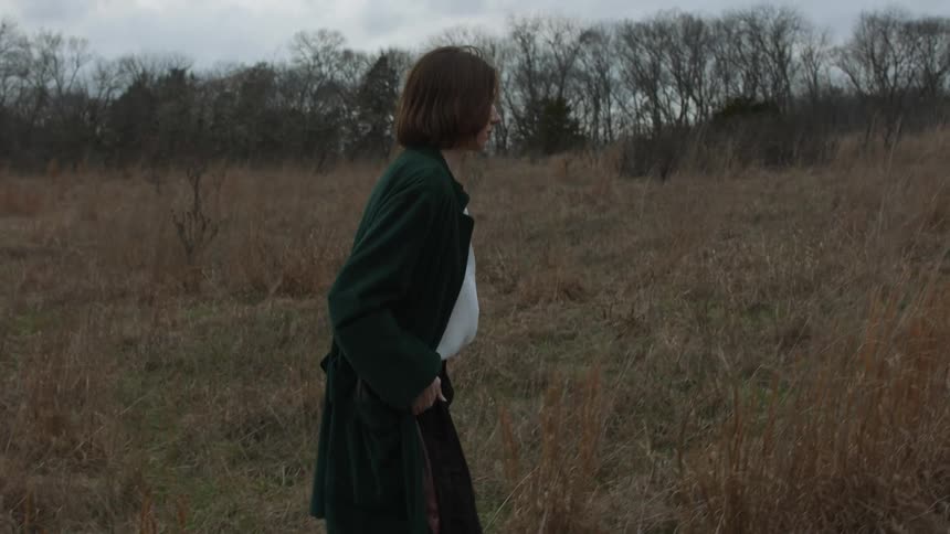 A woman walks through a field in a long coat