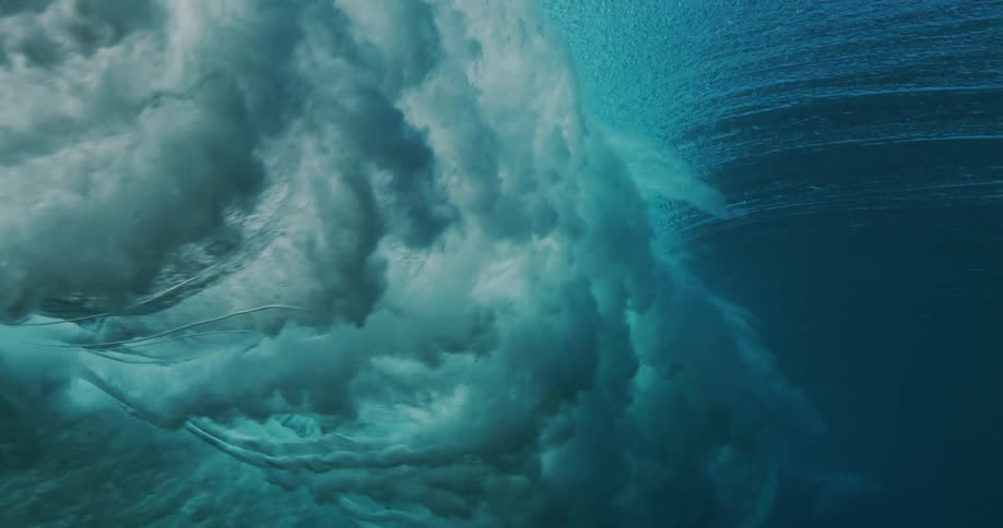 Sunlight shines above the surface and reflects on water splashing as a wave rolls overhead