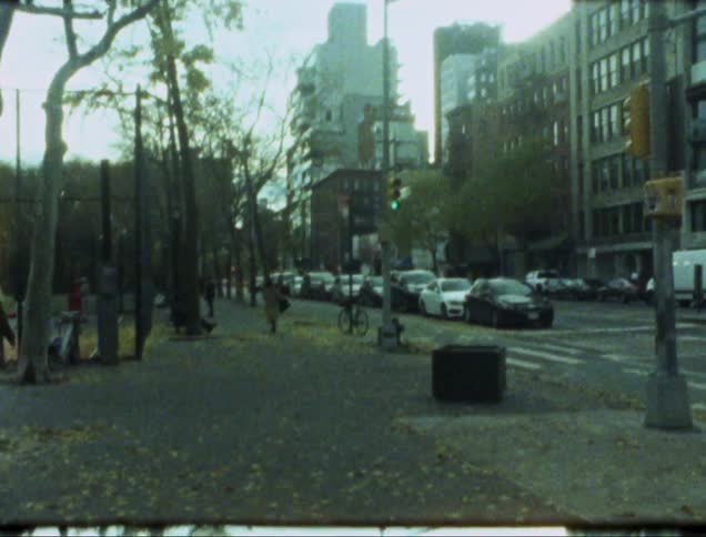 People walk toward a city park past traffic at a downtown intersection