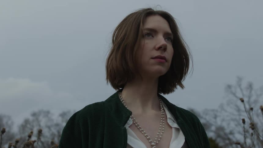 A woman wearing a jacket and necklace standing outside on an overcast day