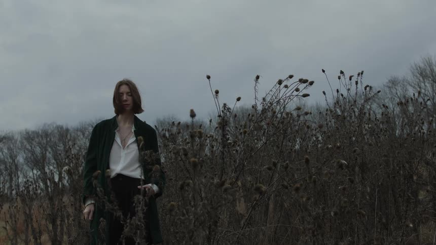 A woman standing with her hand in her pocket in a field of dead plants