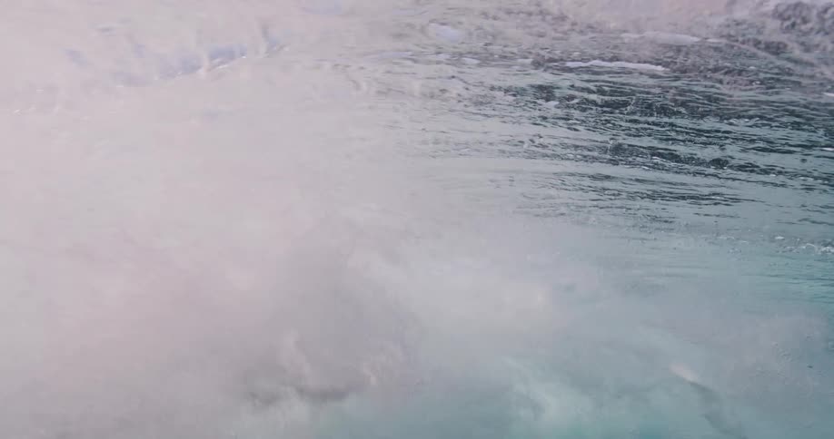 Underwater view looking up as the sunlight reflects on the water surface as a wave rolls overhead
