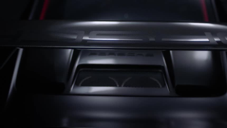 Light shines on the rear spoiler of a gray sports car in the darkness