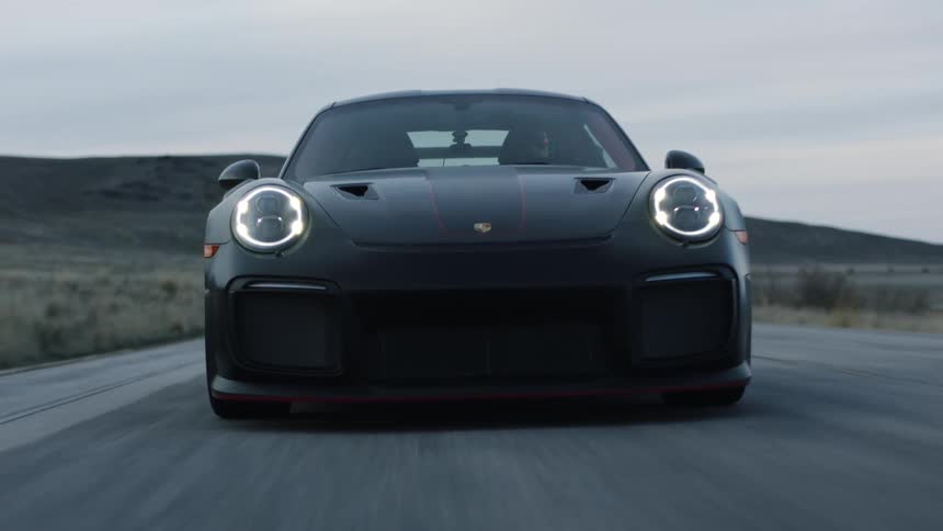 A man driving a sports car speeds down a gravel road