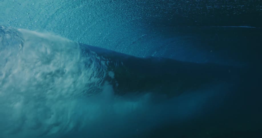 Sunlight shines above the surface and reflects on water splashing as a wave rolls overhead