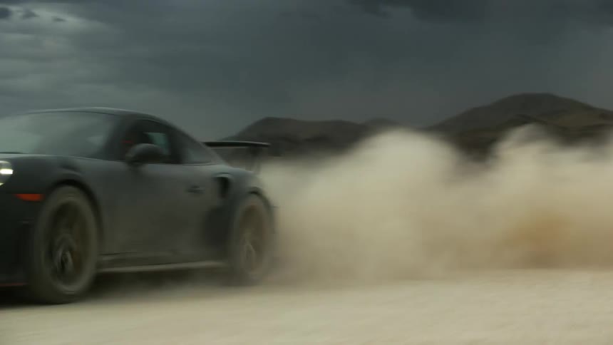 A black sports car driving erratically and kicking up dust in a desert