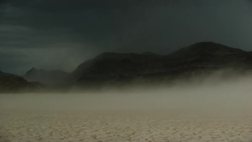 Black car speeding across desert under storm clouds skids and kicks up dust as it turns