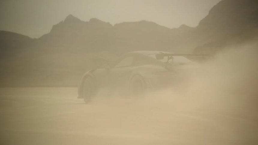 A desert with a black sports car driving fast with mountains in the distance