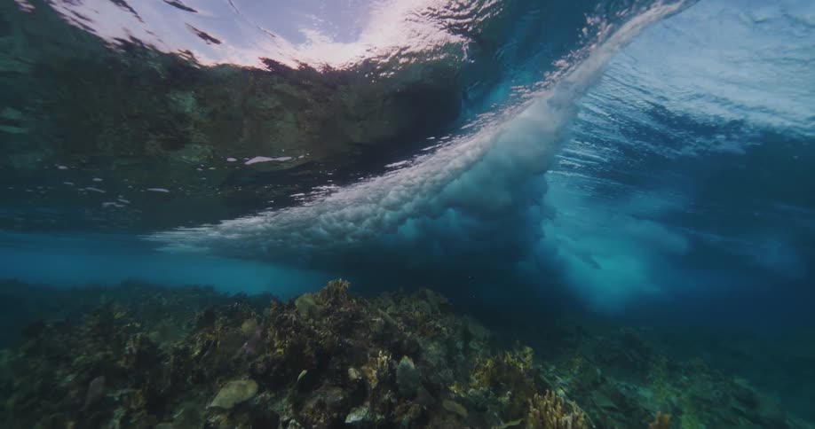 Waves rolling over the top of the ocean with a coral reef below