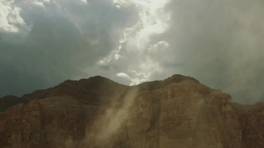 Fog moves across mountains as the sun shines through a cloudy sky
