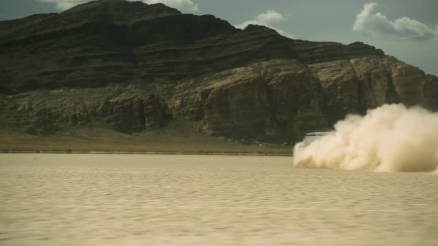Car kicks up dust with mesas in the distance