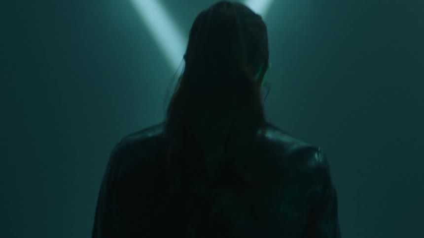 A woman with a long dark ponytail walking in a dimly lit room with spotlights