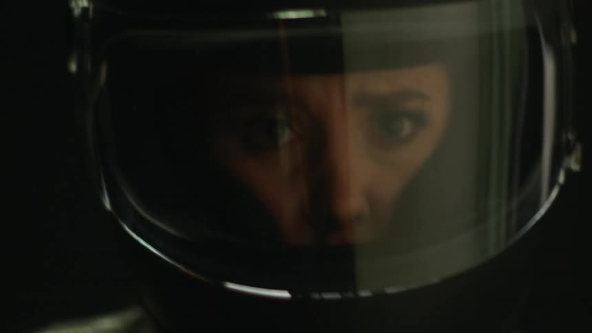 A woman wearing a helmet with a clear face shield furrowing her brow and wincing